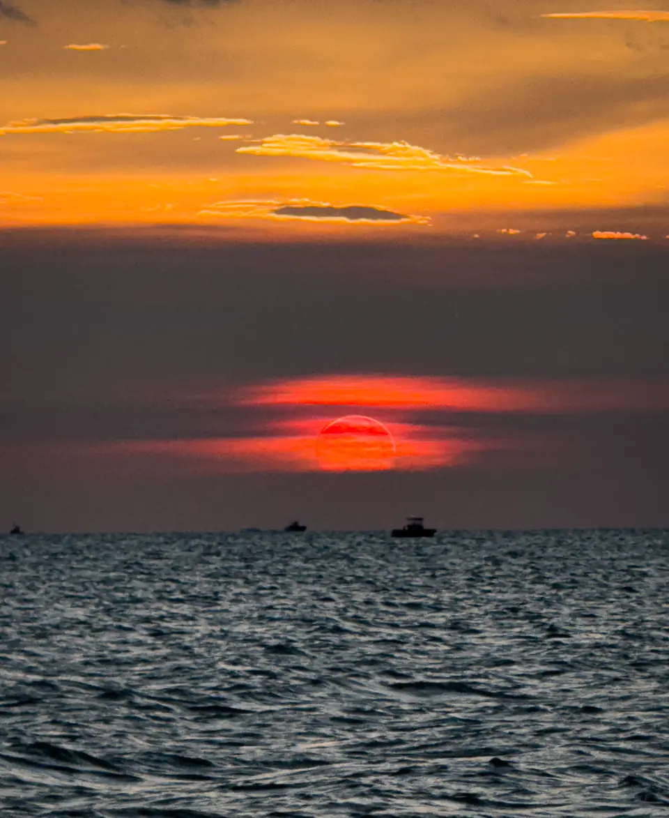 A red sun sinking into the sea off the Florida Keys with boats on the horizon