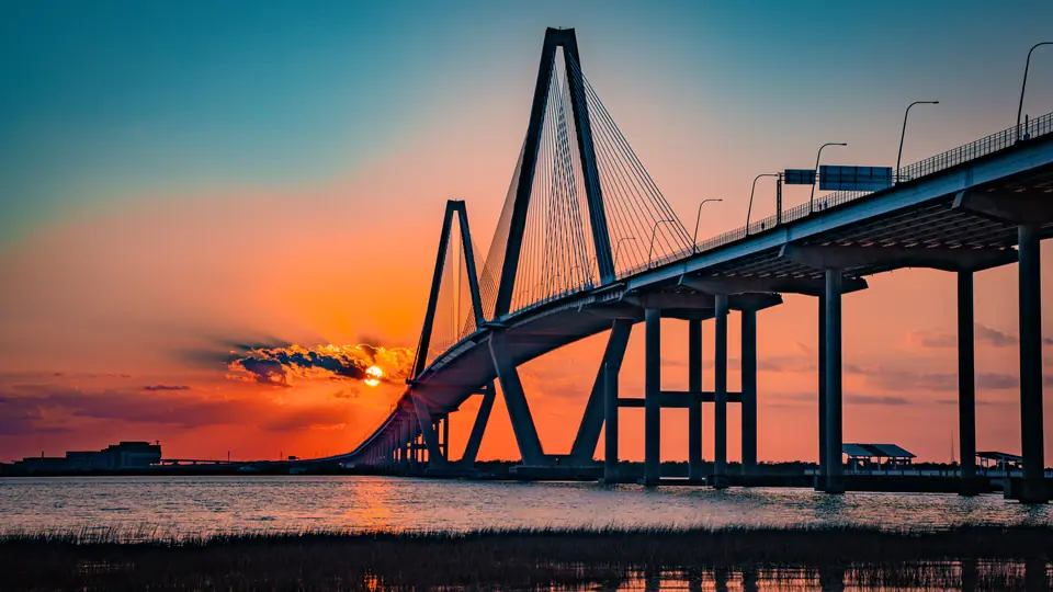 The Ravenel Bridge silhouetted against an orange sunset over the Cooper River in Charleston, SC